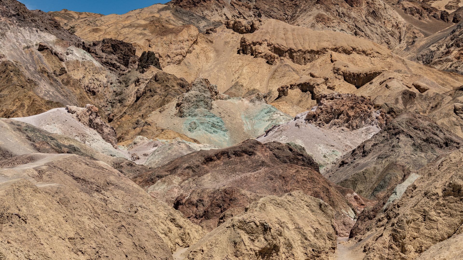 A panoramic view of Artists Palette in Death Valley National Park, showcasing colorful hills with vibrant hues of red, orange, yellow, green, and purple, resulting from mineral oxidation in the volcanic deposits of the Black Mountains.