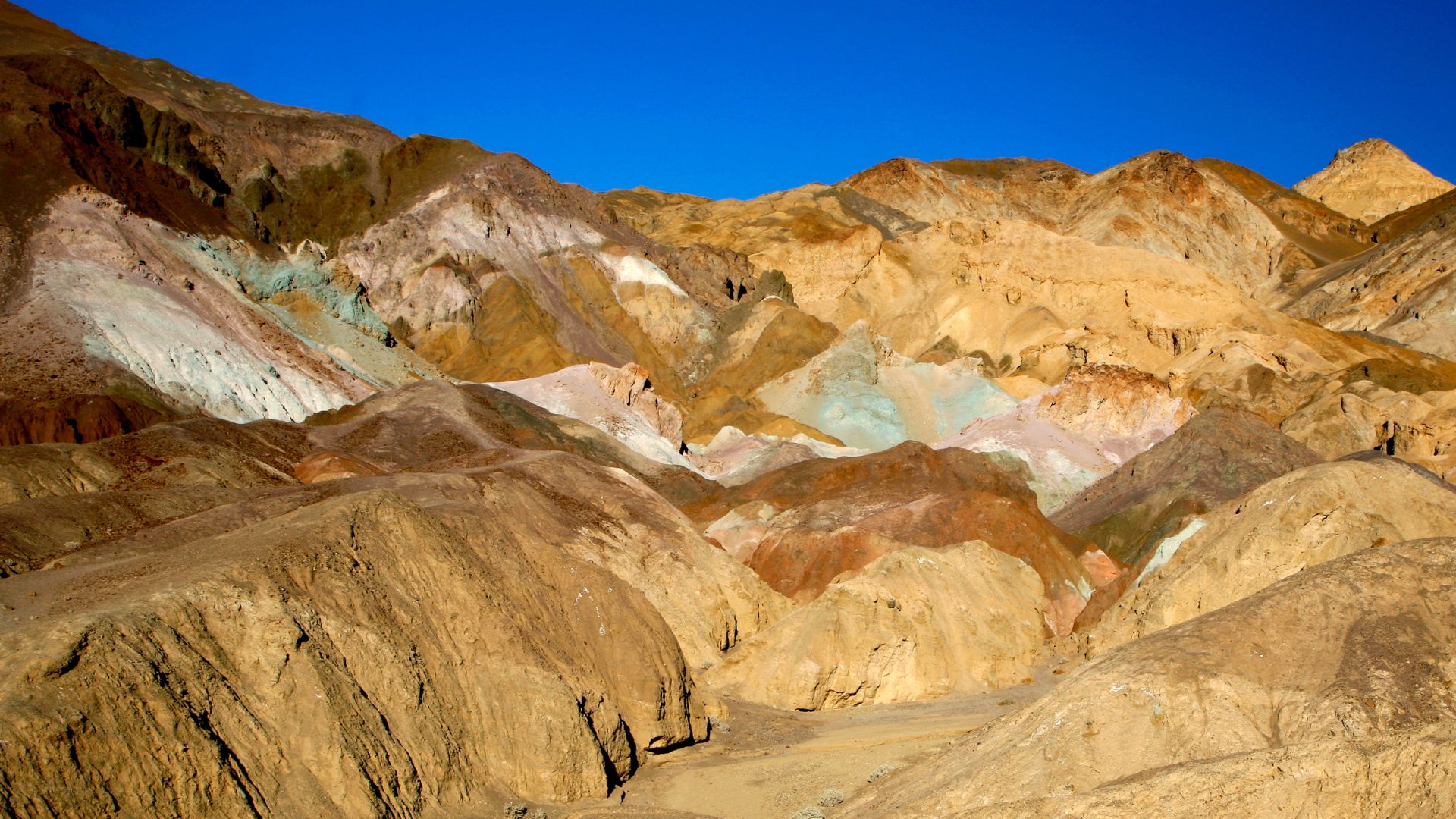 A wide shot of the colorful, eroded hills of Artists Palette in Death Valley National Park, showcasing a spectrum of natural hues under a clear blue sky. 
