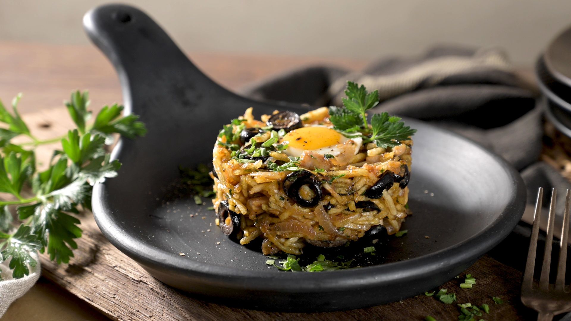 A close-up shot of Bacalhau à Brás, a Portuguese dish made with shredded cod, potatoes, eggs, and olives, plated on a black dish.