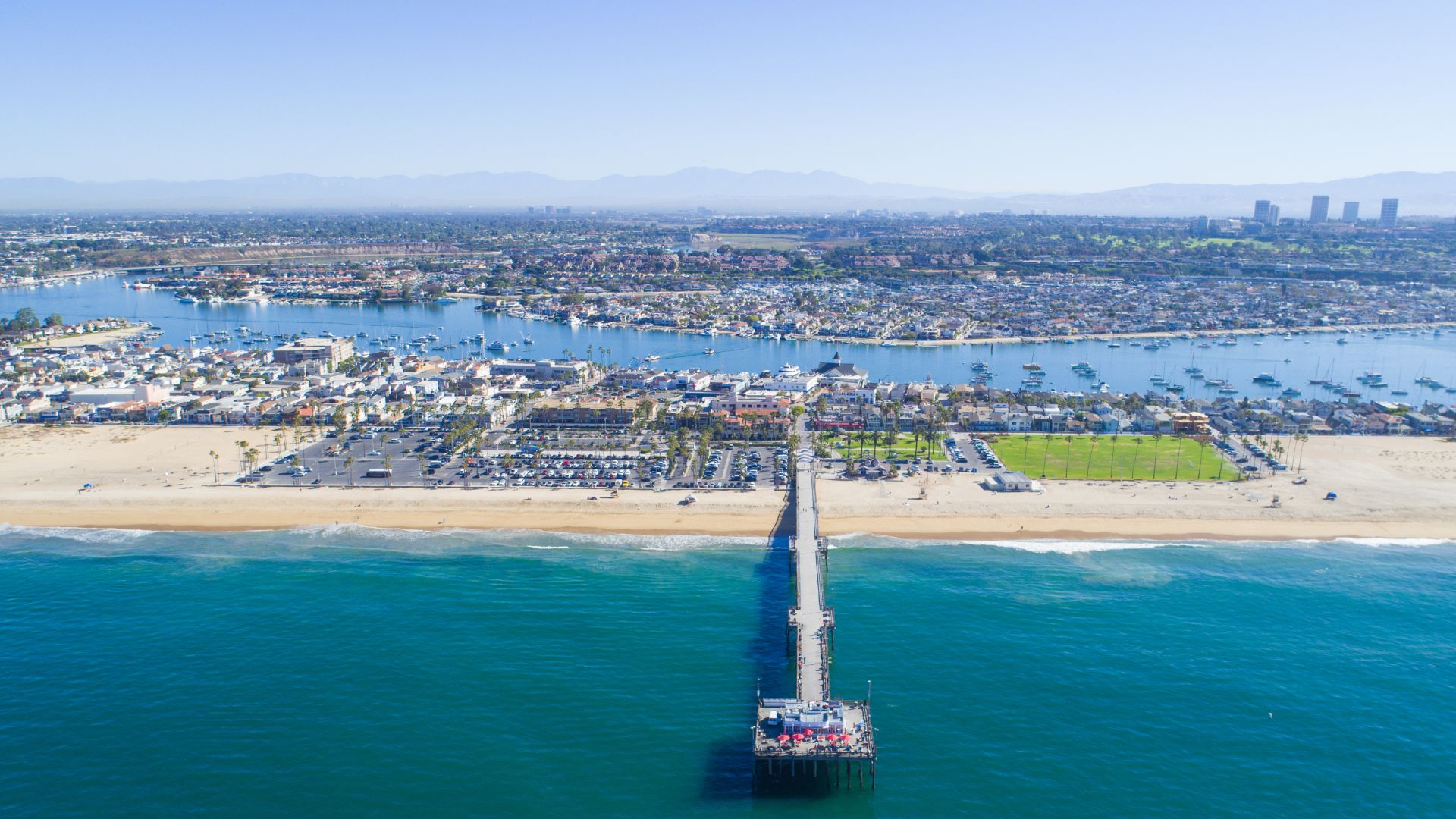 Aerial view of Balboa Pier and Newport Beach coastline in Southern California, showcasing the pier extending into the Pacific Ocean with harbor and city in the background.