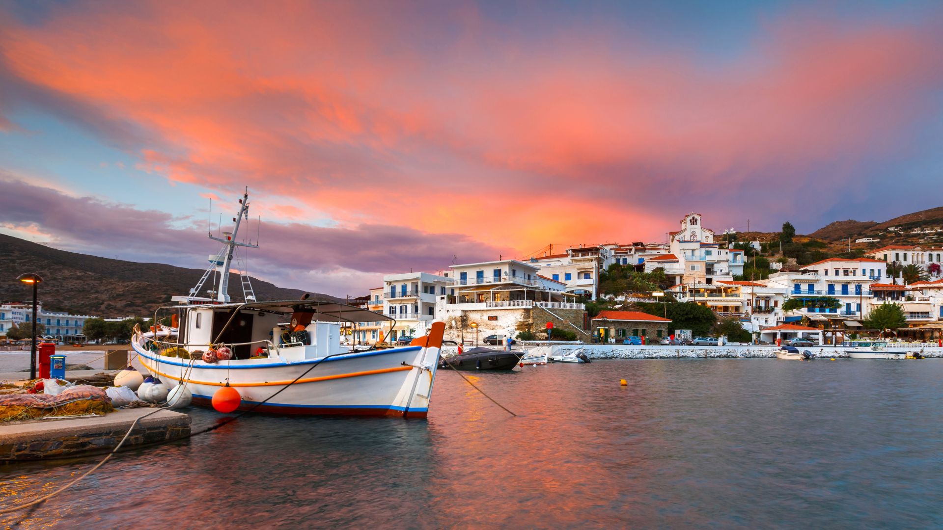 Sunset view of Batsi village in Andros, Greece, with a fishing boat in the foreground.