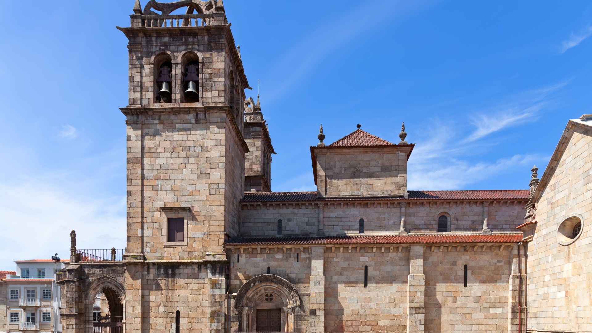 A stone cathedral with a prominent bell tower and multiple architectural styles under a clear blue sky.