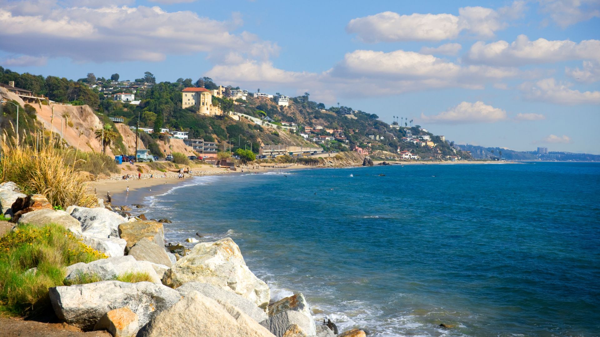 Panoramic view of Carbon Beach in Malibu, California, showcasing the Pacific Ocean, sandy shore, and beachfront homes nestled against the bluffs under a clear sky.