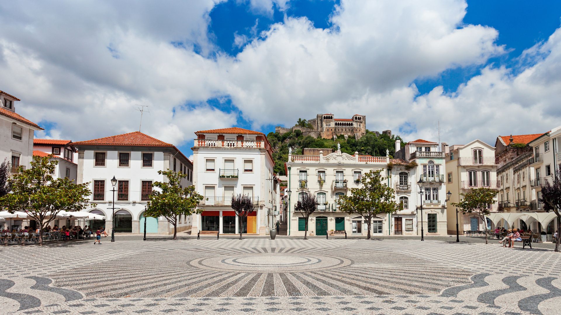Central square of Leiria, Portugal, featuring historic buildings and the medieval Castelo de Leiria under a blue sky with clouds.