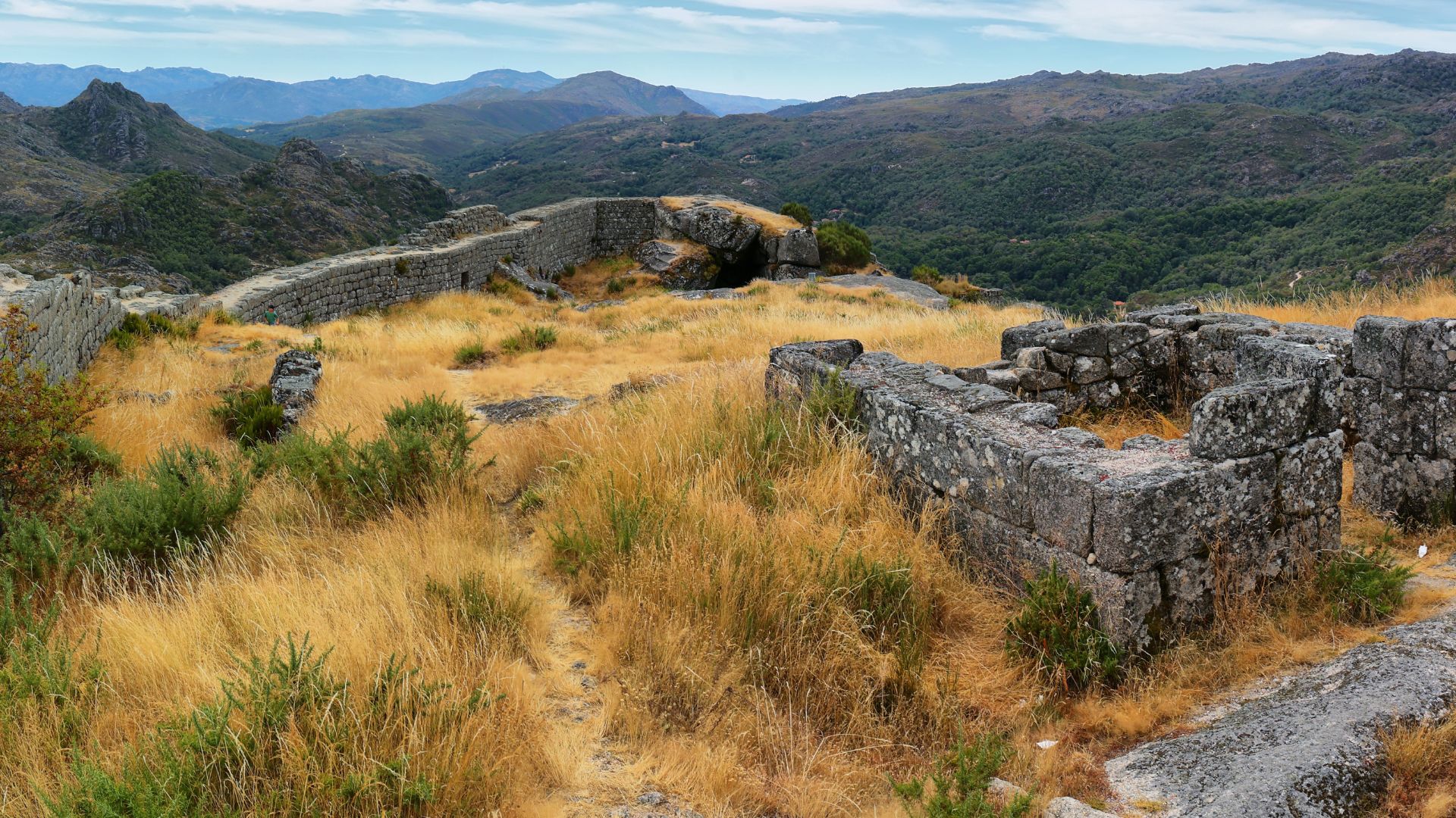 Ruins of Castro Laboreiro Castle on a hillside with dry grass and distant mountains in Peneda-Gerês National Park, Portugal.