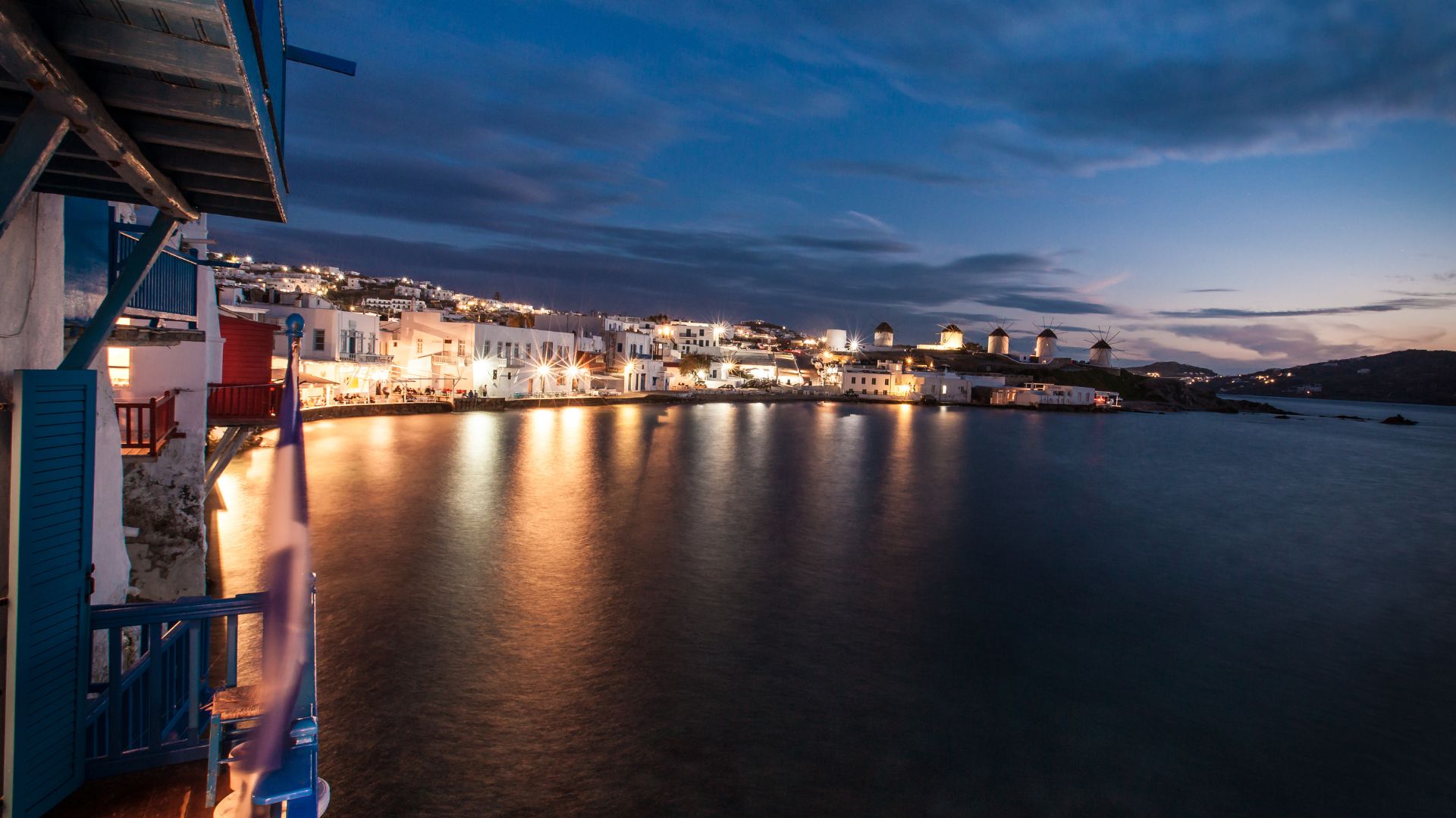 Night view of Mykonos town waterfront with white buildings and windmills.