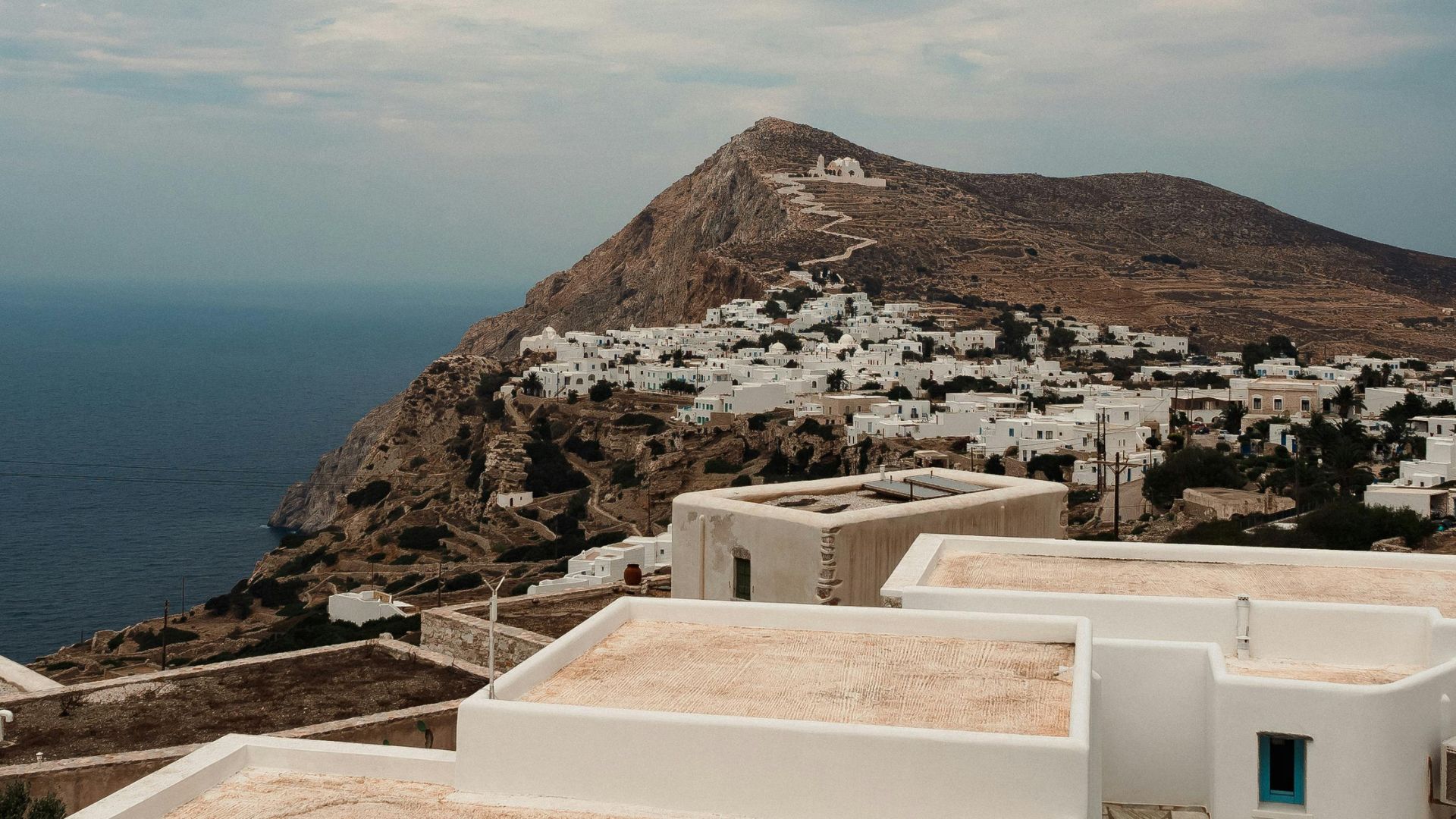 Whitewashed church on a hill with a winding path leading up to it in Folegandros, Greece.