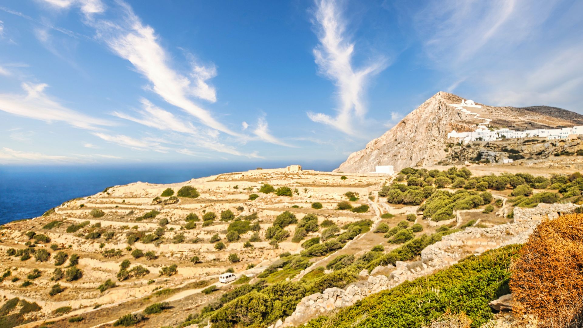 Cliffside village of Chora in Folegandros, Greece, with terraced hills and blue sea.
