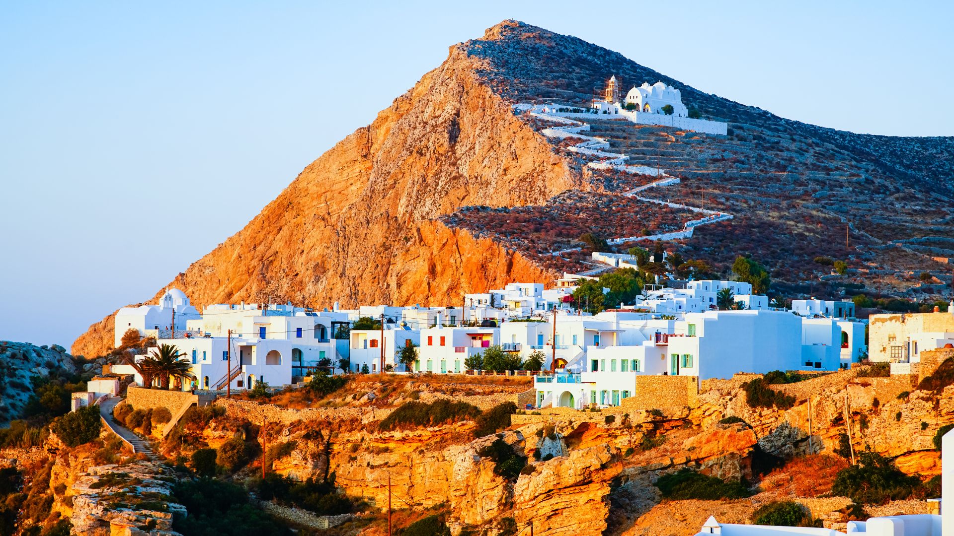 Whitewashed church on a hill with a winding path leading up to it in Folegandros, Greece on sunset.
