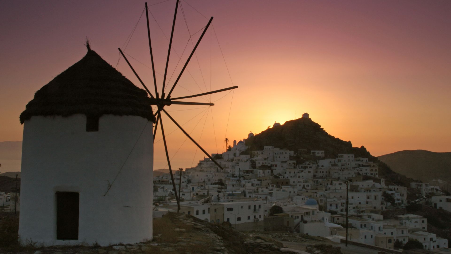 Sunset view of Chora village and a traditional windmill in Ios, Greece.