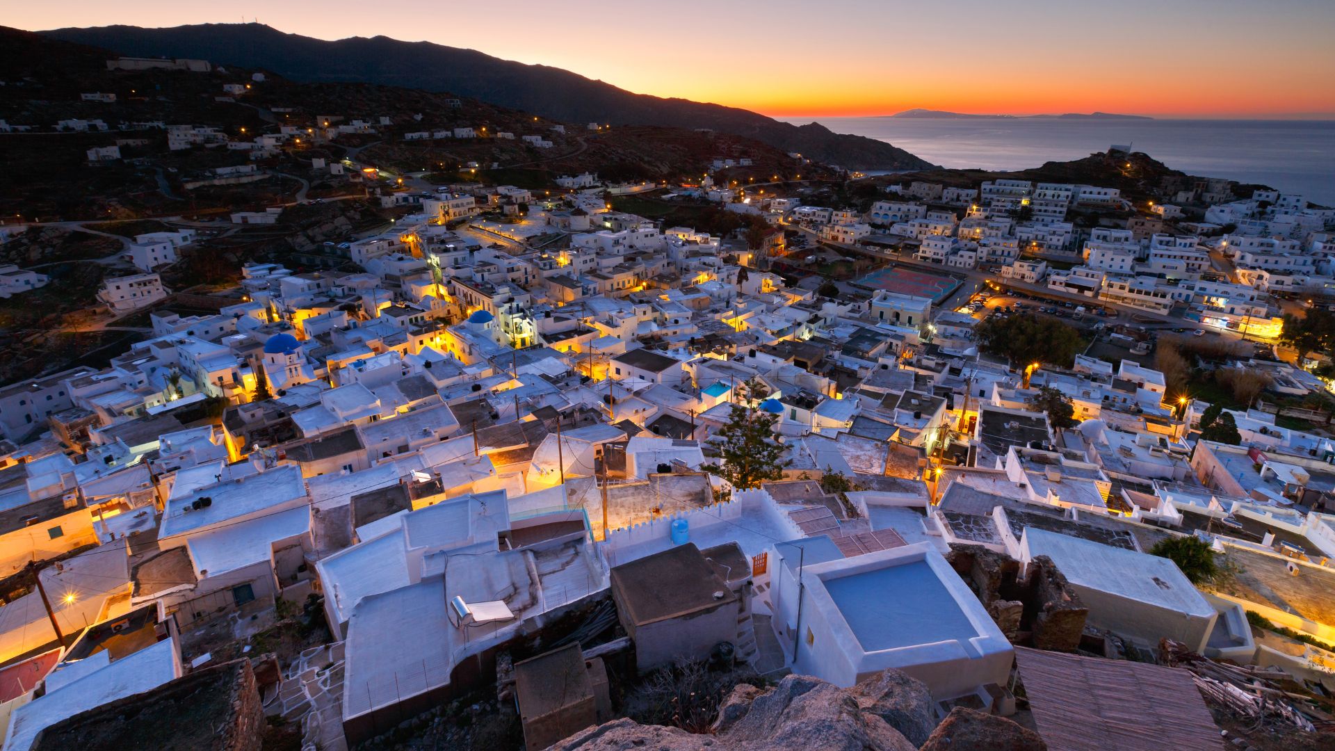 Sunset over Chora, Ios, Greece, with white buildings and sea view.