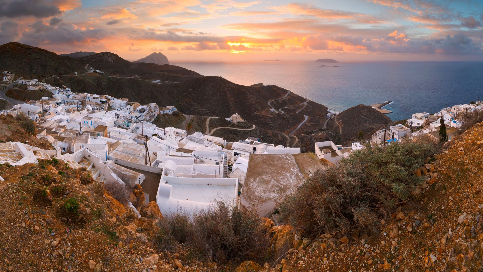Anafi, Greece: Whitewashed Cycladic village perched on hills overlooking the Aegean Sea at sunset.