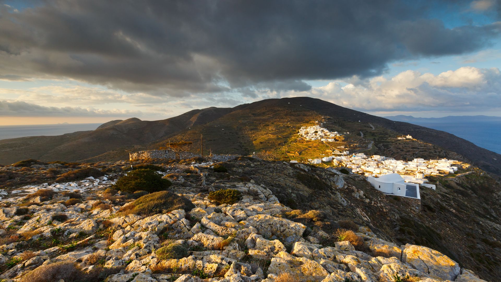 Sikinos Chora village, Greece: Panoramic view of the traditional Cycladic settlement on a hillside under a dramatic sky.