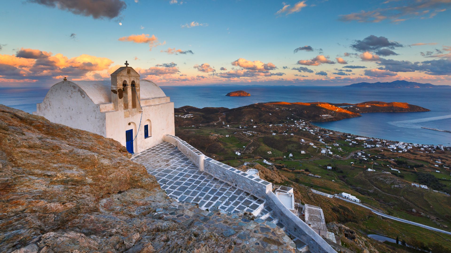 A white church with a blue door sits atop a hill overlooking the sea in Serifos, Greece.