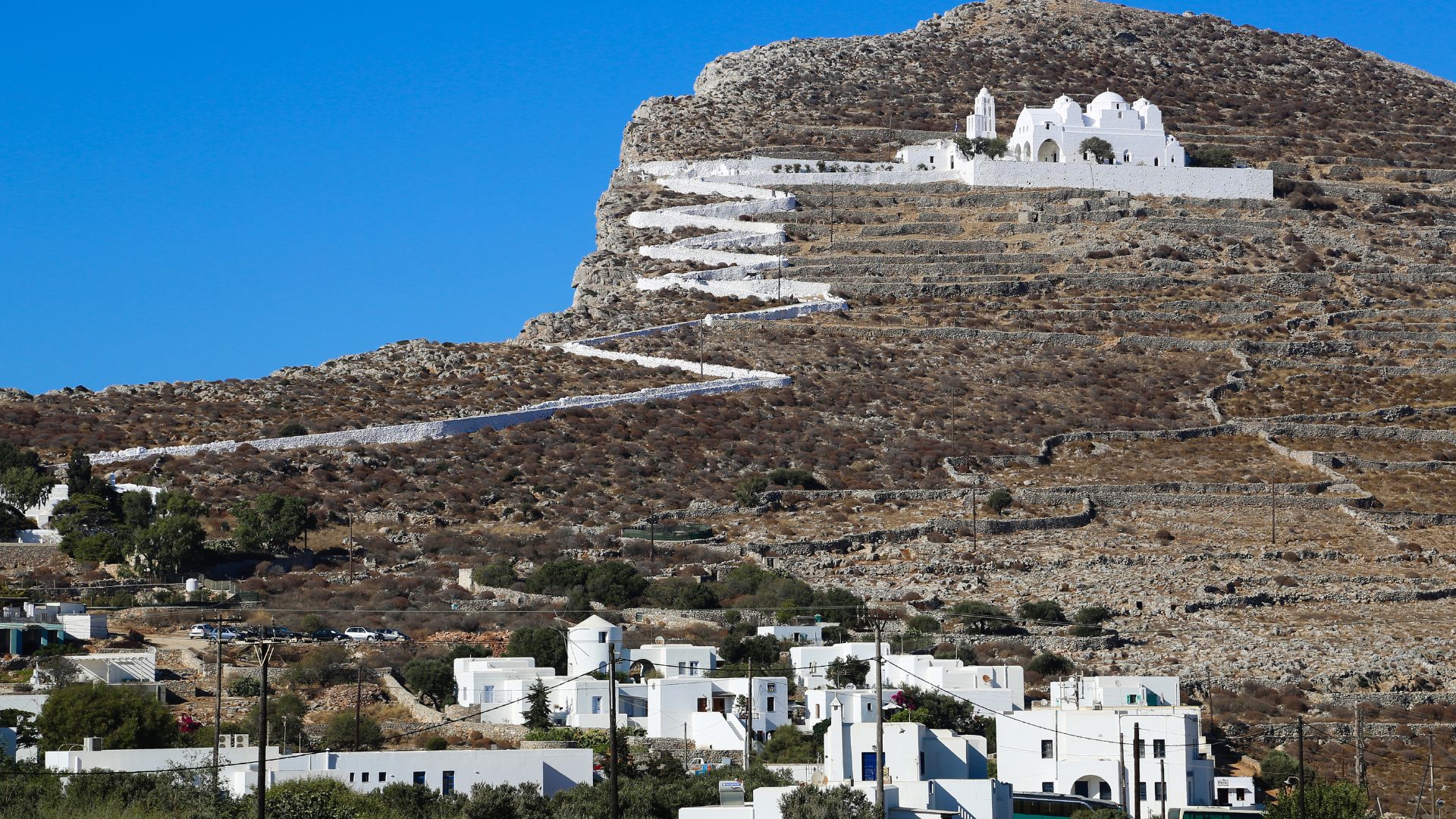 Whitewashed church on a hill with a winding path leading up to it in Folegandros, Greece.