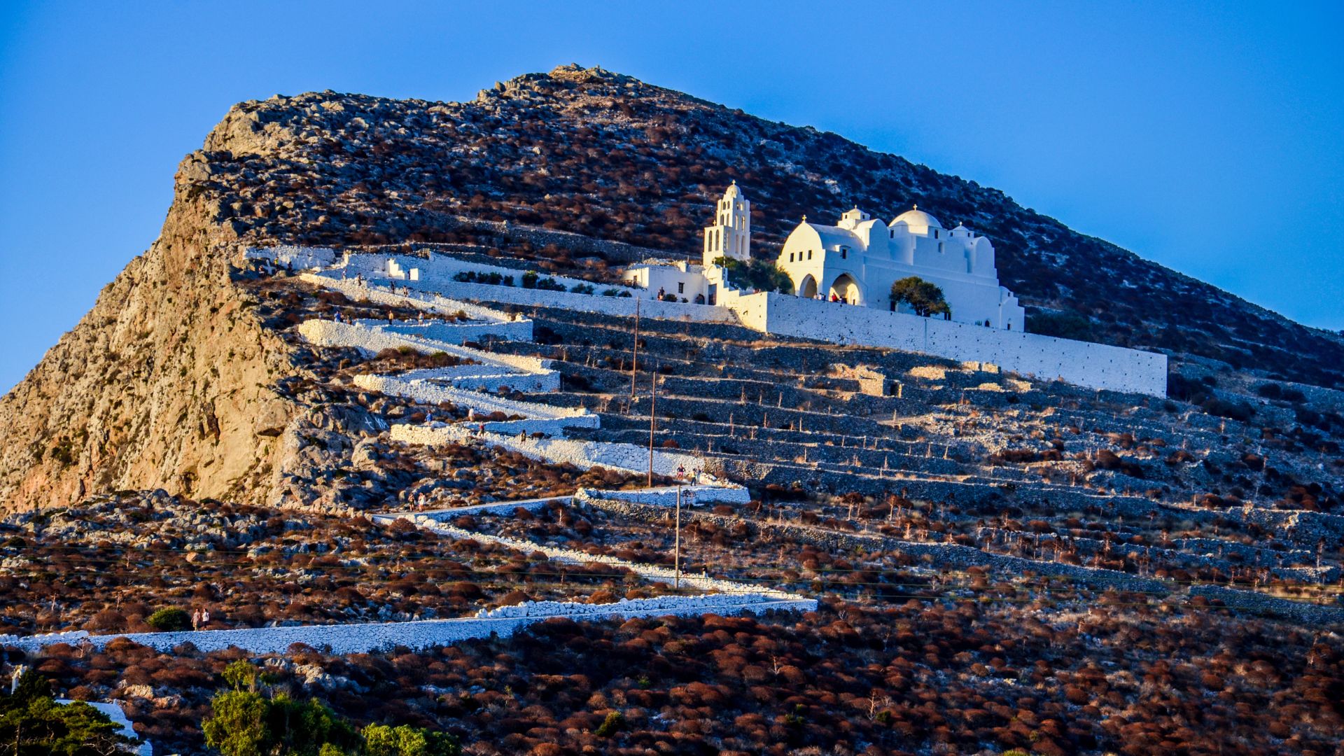 Whitewashed church on a hill with a winding path leading up to it in Folegandros, Greece on sunset.