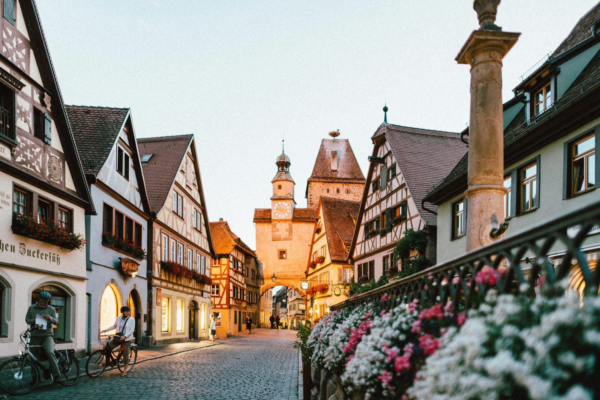 Close-up of delicate pink and white flowers on a black metal fence, with Rothenburg ob der Tauber’s historic buildings