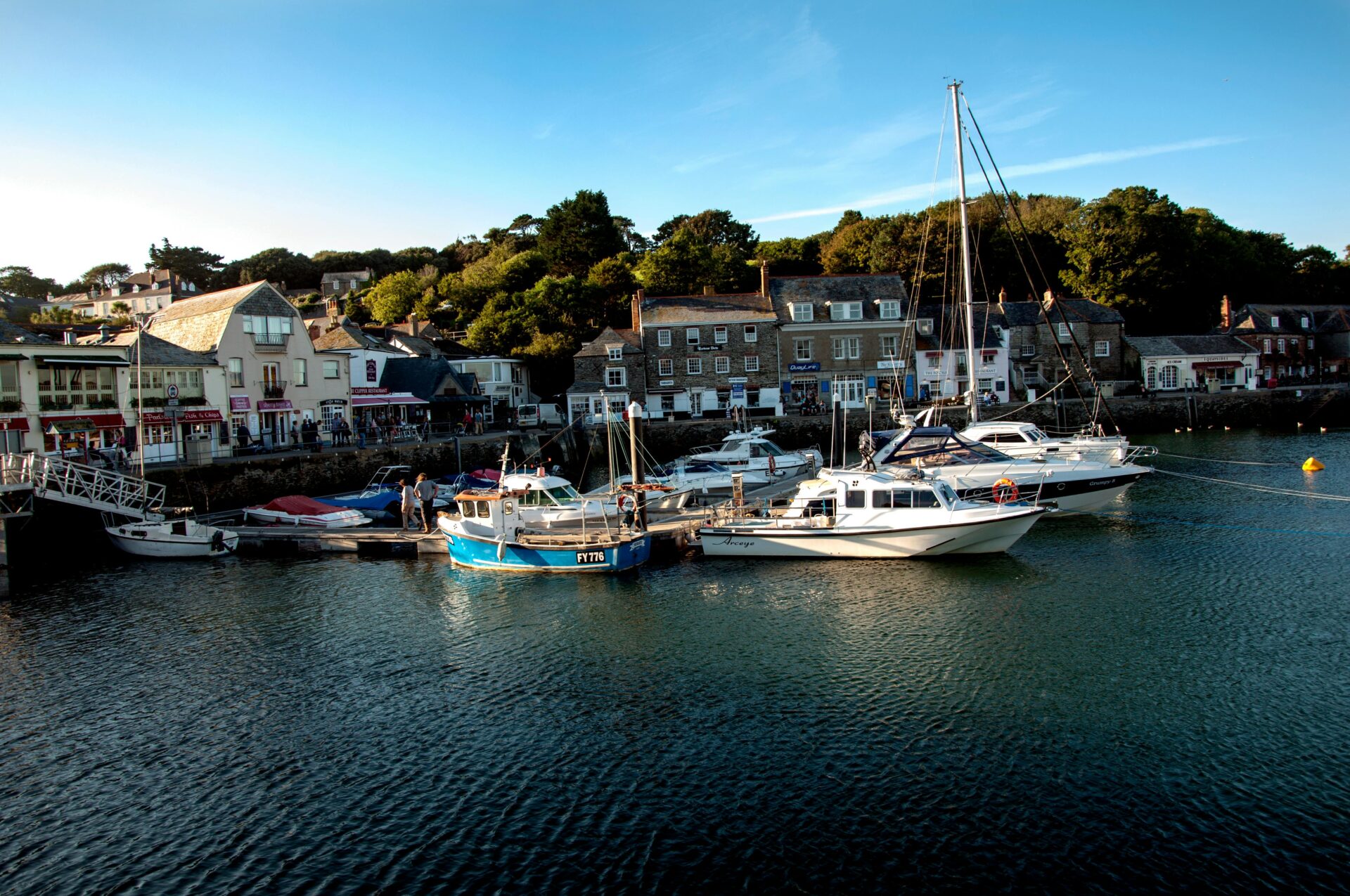 Colorful boats anchored near the shore, with traditional buildings lining the coastline of Cornwall