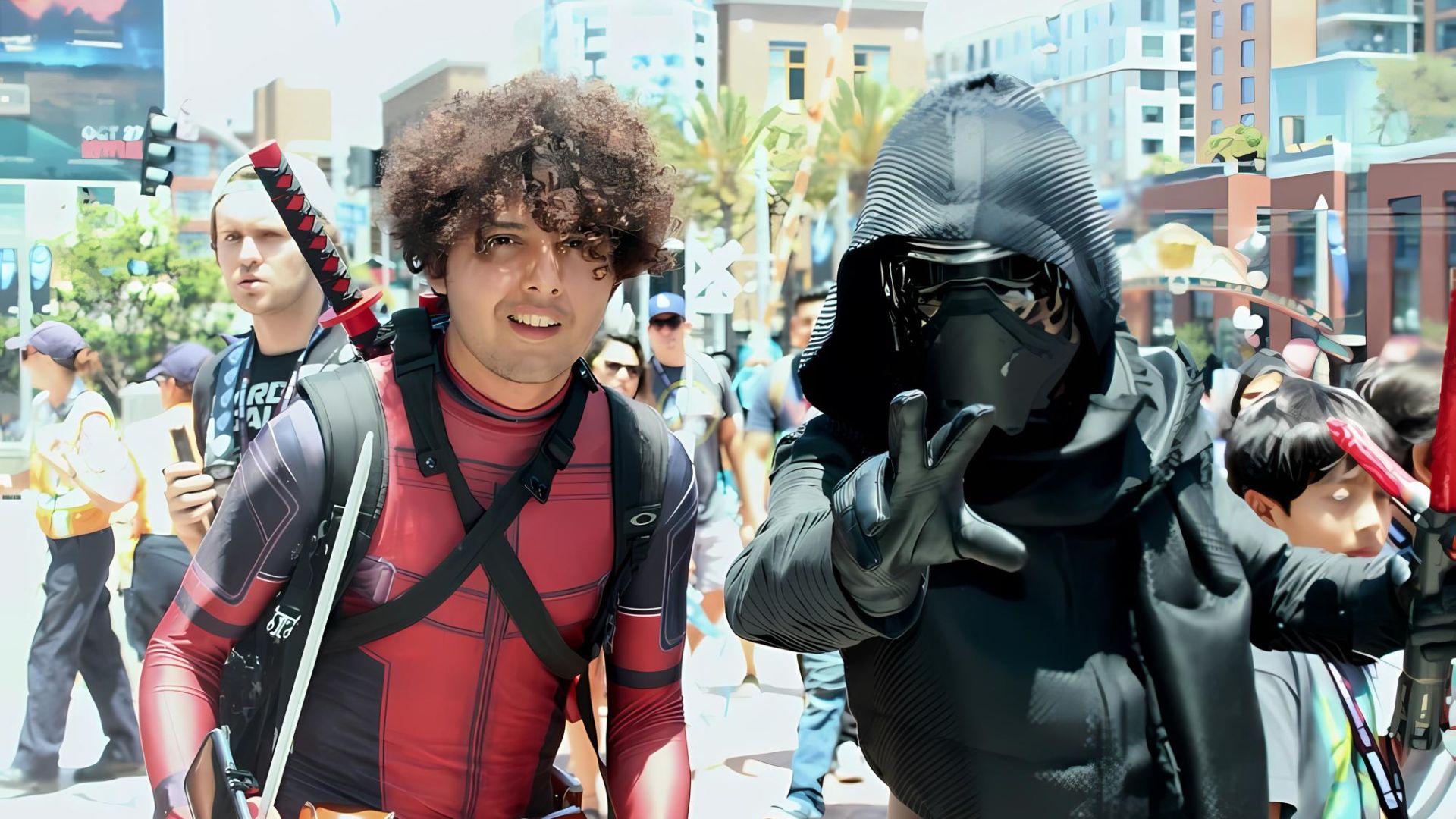 A man in a Deadpool costume with curly hair and a man in a Kylo Ren costume with a mask and hood pose outdoors among a crowd of people.