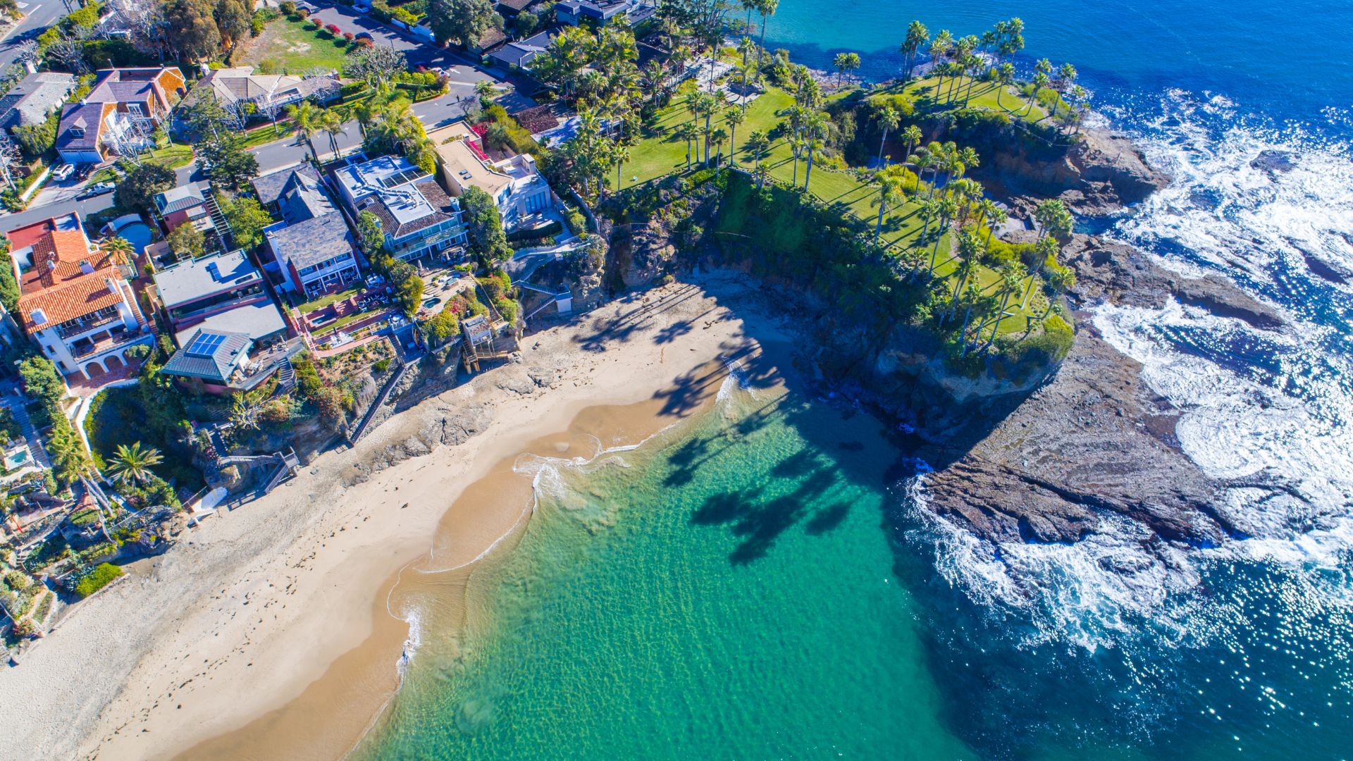 Aerial view of Laguna Beach, California, showcasing the scenic coastline, sandy beaches, turquoise ocean, and a residential area nestled along the cliffs in Orange County.