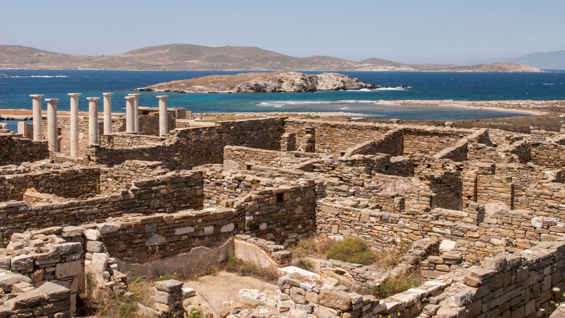 Ancient ruins on Delos Island, with a view of the sea and distant hills.