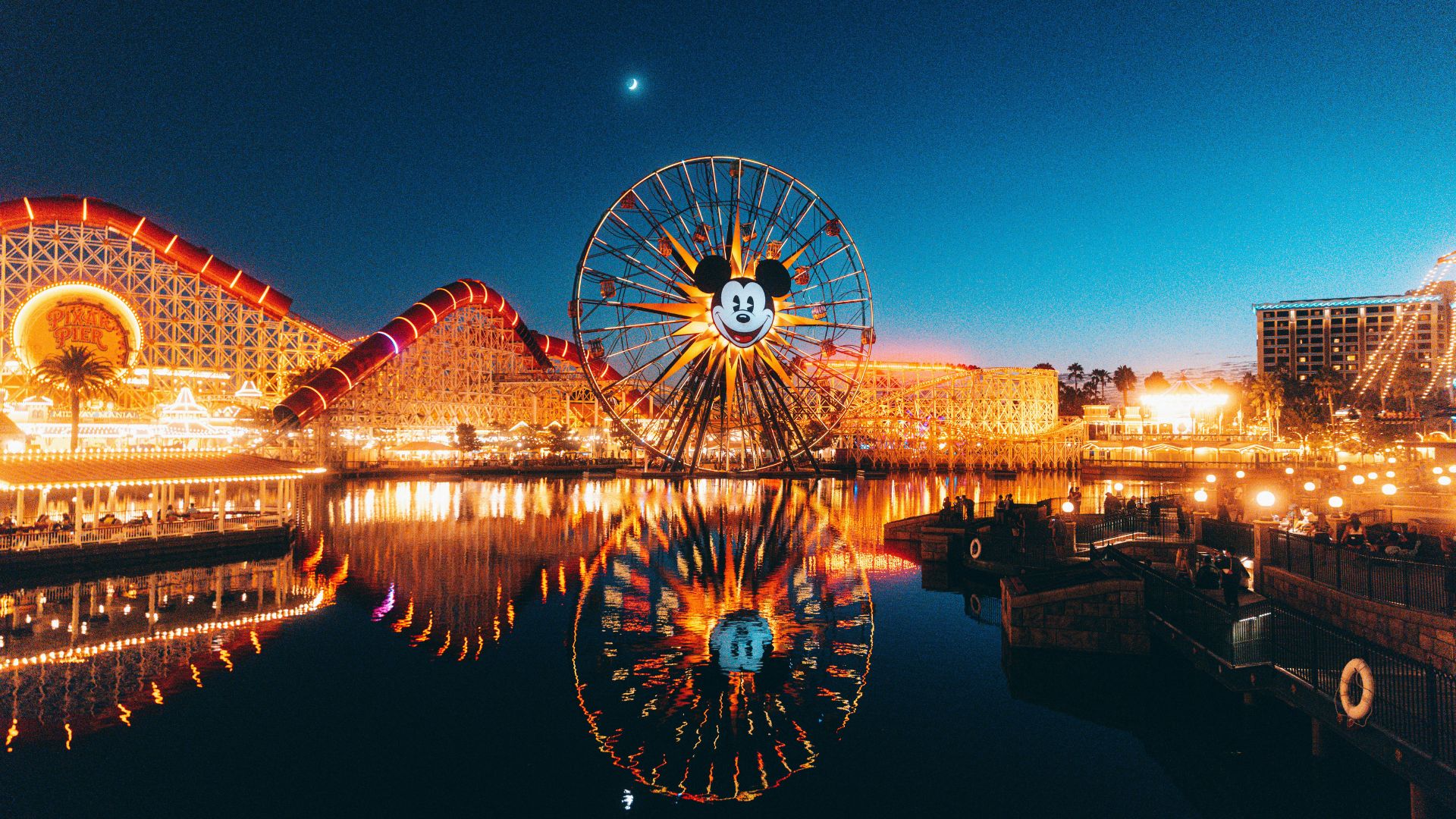 Pixar Pal-A-Round Ferris wheel and Incredicoaster at Disney California Adventure Park at dusk with lights reflecting on the water