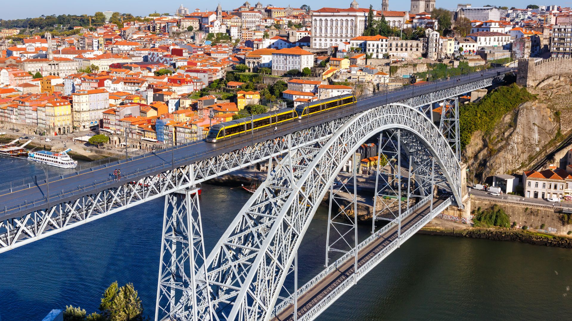 Dom Luís I Bridge spanning the Douro River in Porto, Portugal, connecting Porto and Vila Nova de Gaia with boats docked along the riverbank.
