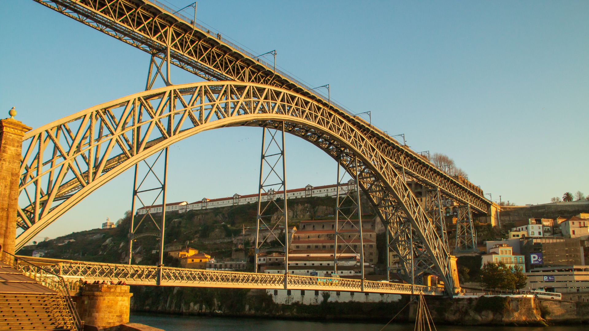 Dom Luís I Bridge spanning the Douro River in Porto, Portugal, connecting Porto and Vila Nova de Gaia with boats docked along the riverbank.