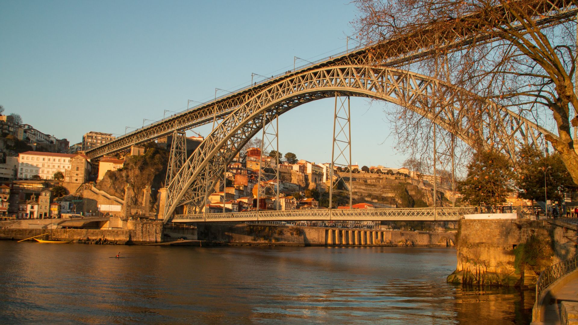 Dom Luís I Bridge spanning the Douro River in Porto, Portugal, connecting Porto and Vila Nova de Gaia with boats docked along the riverbank.