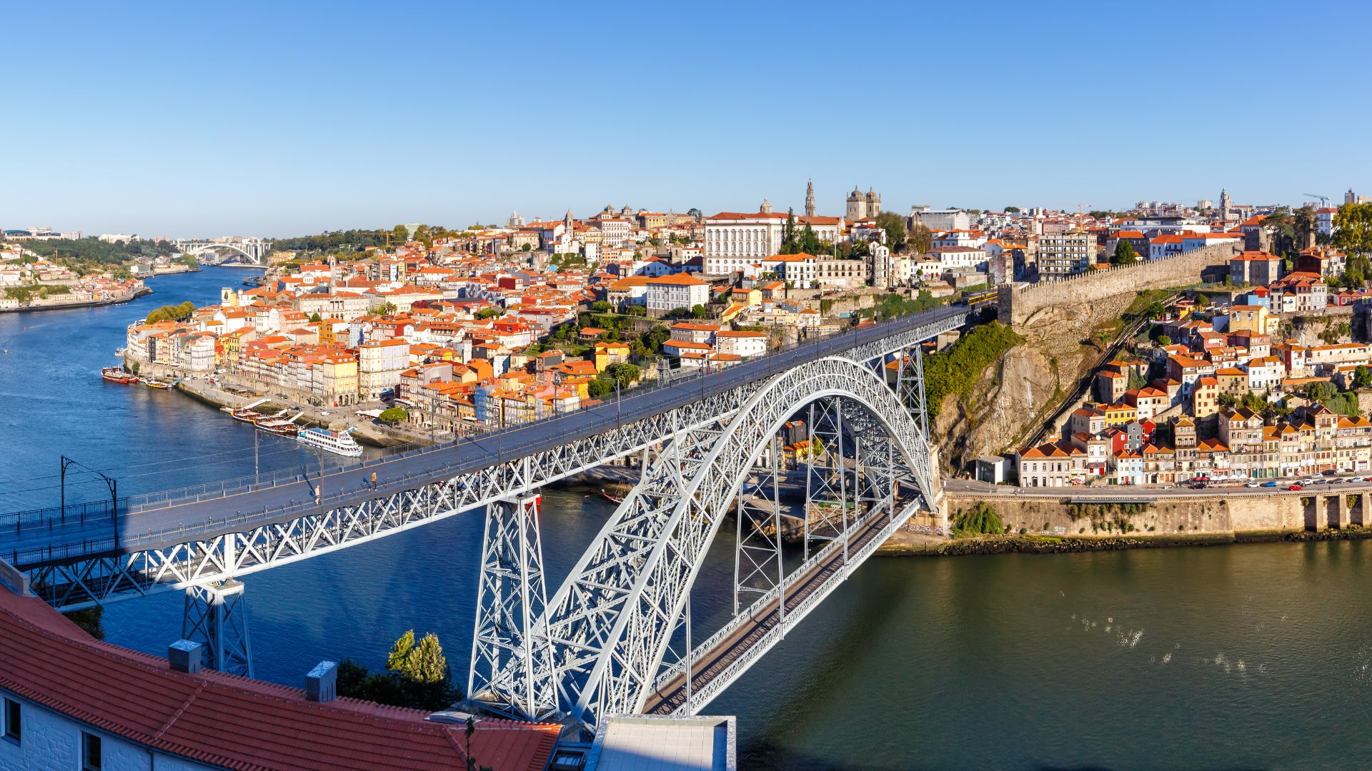 Dom Luís I Bridge spanning the Douro River in Porto, Portugal, connecting Porto and Vila Nova de Gaia with boats docked along the riverbank.