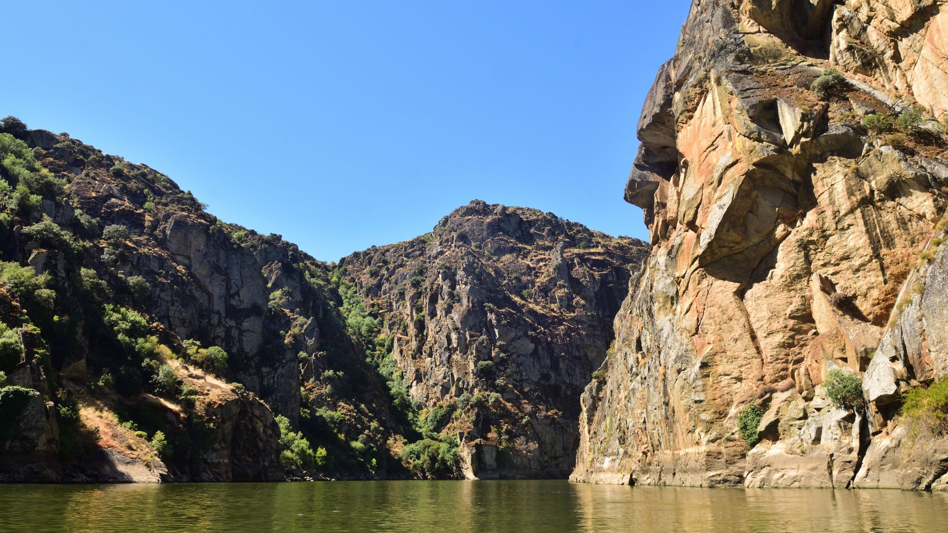 A wide shot of a river winding through a deep, rocky gorge with steep, tree-covered cliffs under a clear blue sky.