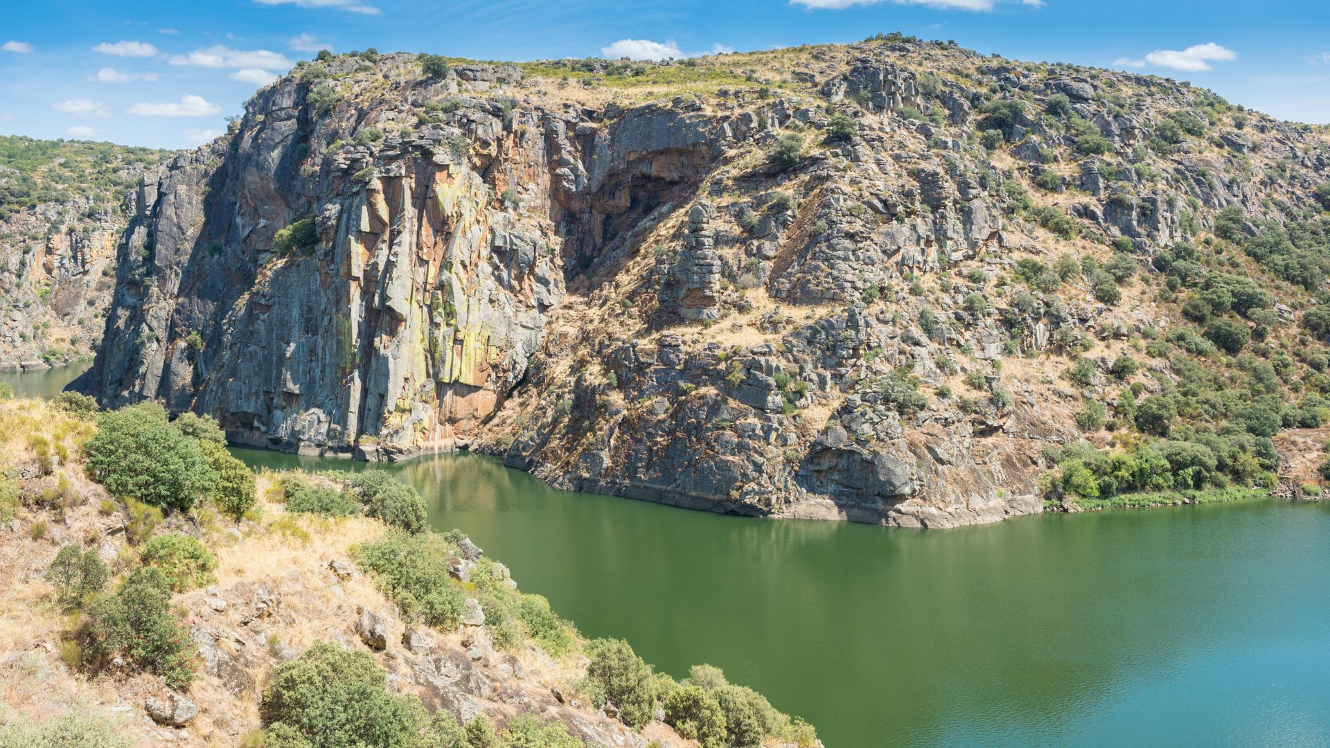 A wide shot of a river winding through a deep, rocky gorge with steep, tree-covered cliffs under a clear blue sky.