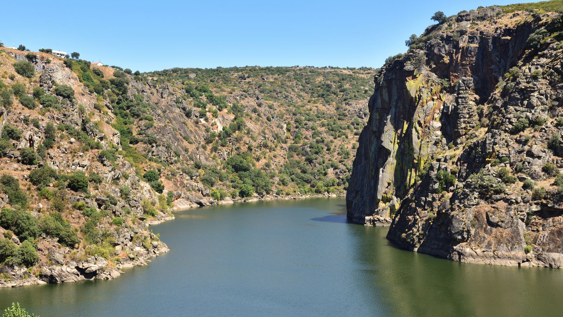 A wide shot of a river winding through a deep, rocky gorge with steep, tree-covered cliffs under a clear blue sky.