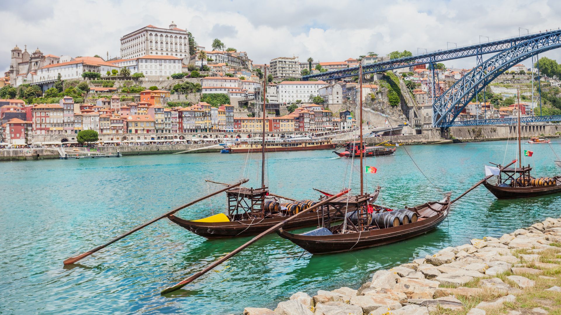 Traditional Rabelo boats on the Douro River in Porto, Portugal, with the iconic Dom Luís I Bridge and the historic city skyline in the background.