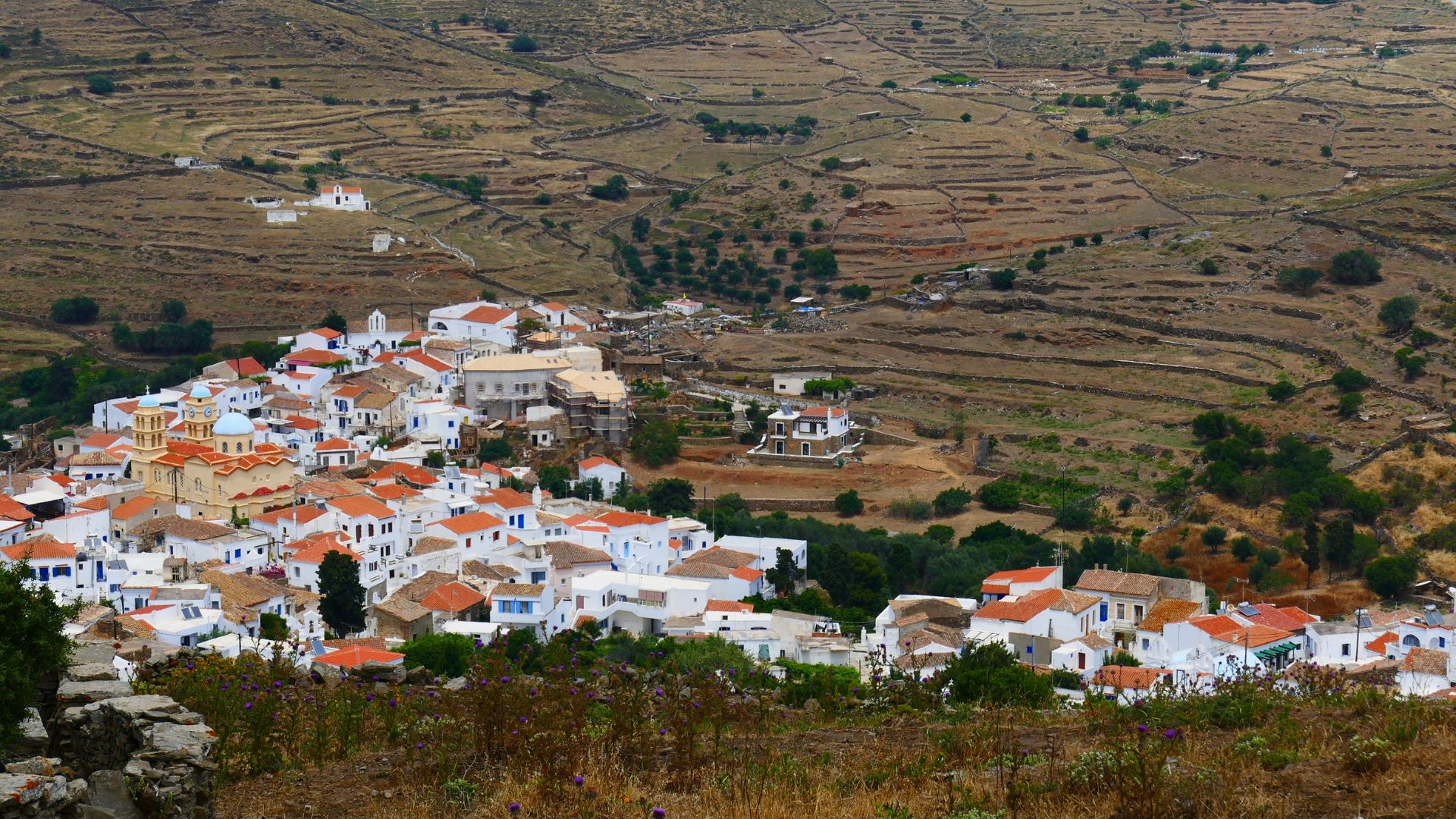 Aerial view of Dryopida village in Kythnos, Greece, featuring white houses with tiled roofs nestled in a valley with terraced hillsides.