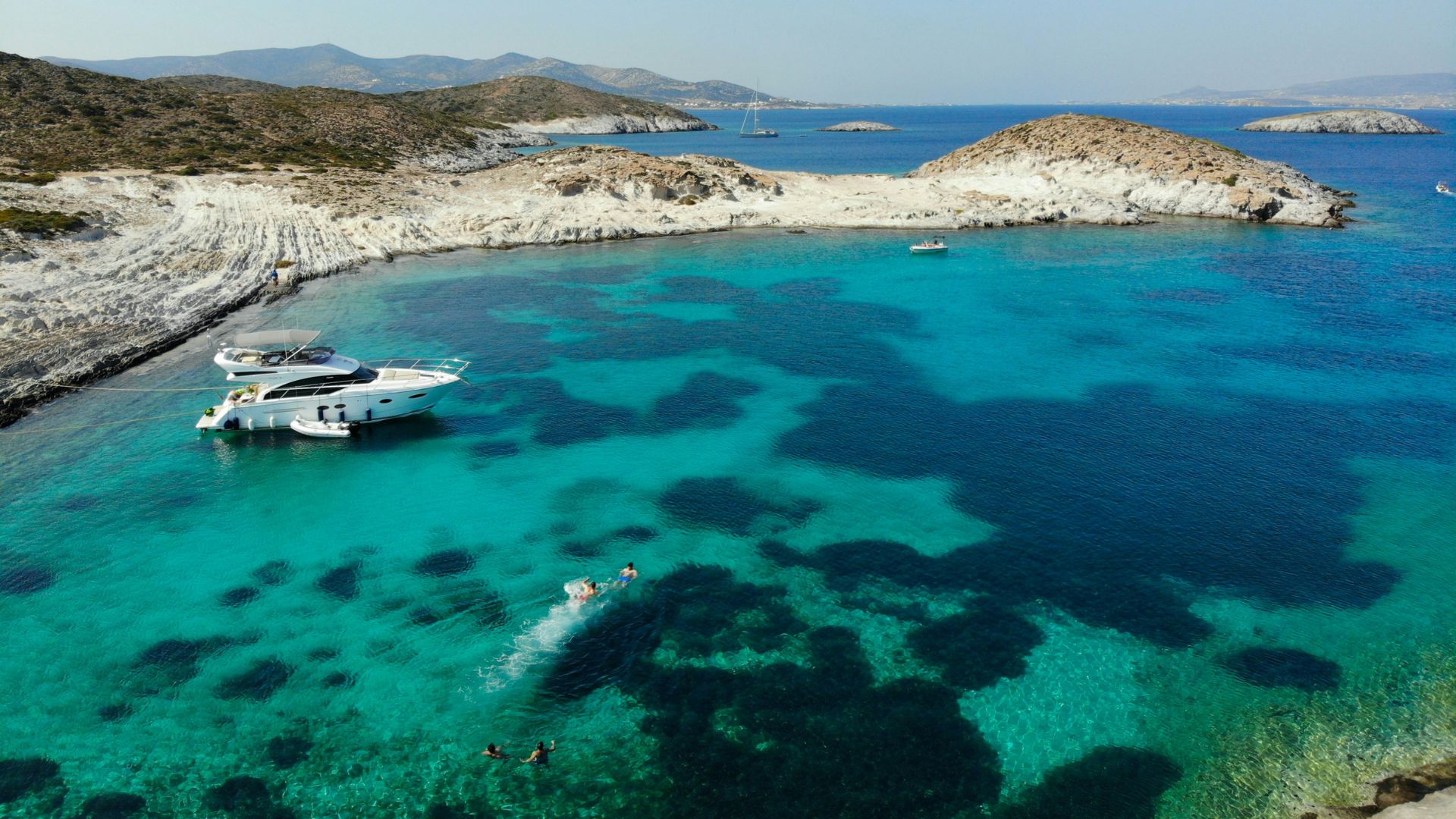 Scenic view of Faneromeni Beach in Antiparos, Greece, with turquoise waters and a yacht.