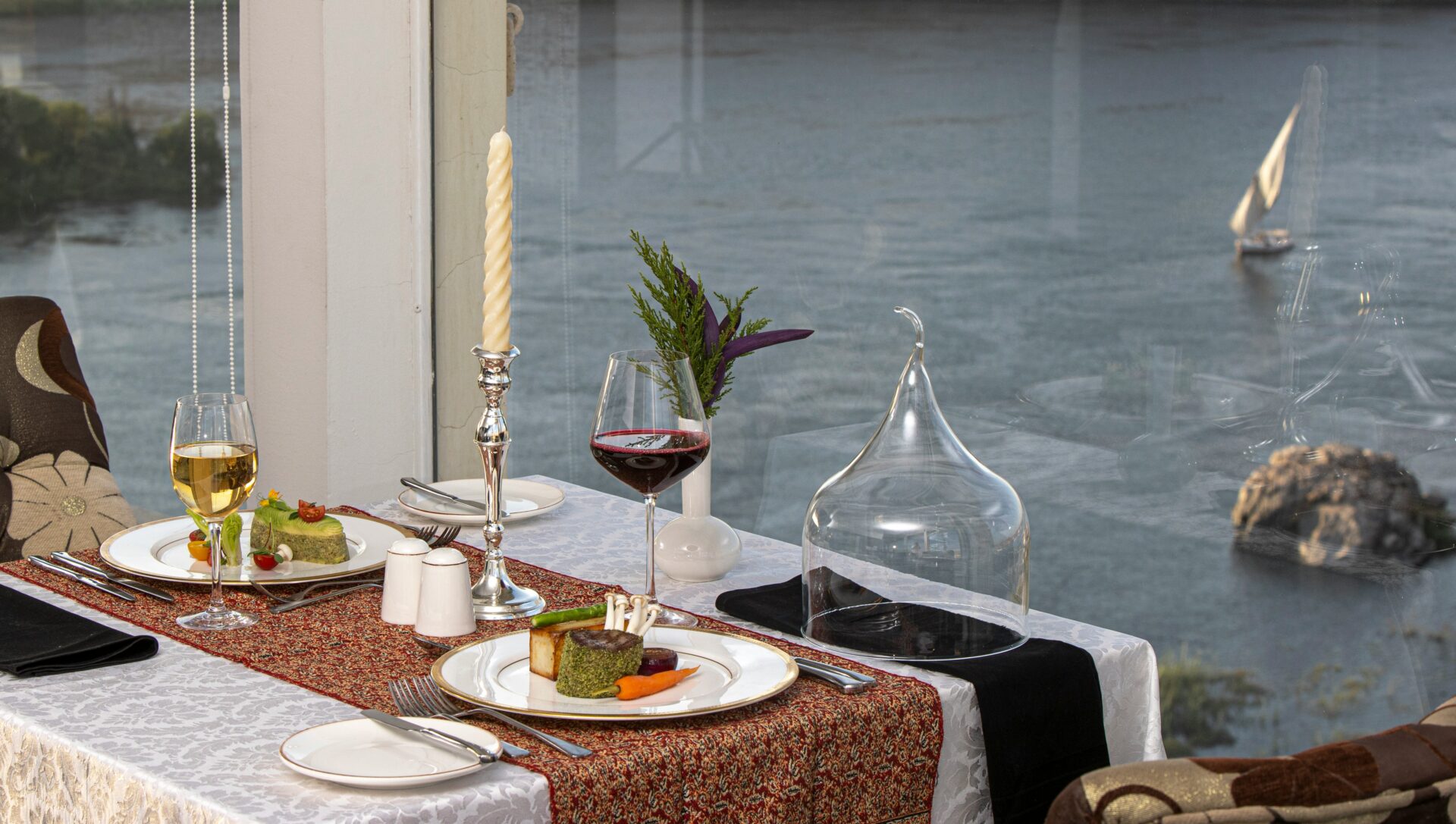 Fine dining table with gourmet food and glasses of wine - reflection of a lake
