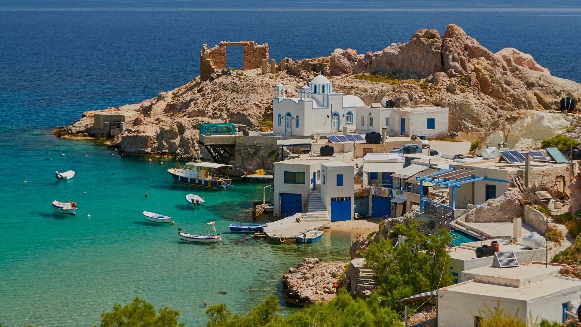 Firopotamos Beach, Milos Island, Greece, with colorful boats and whitewashed buildings.