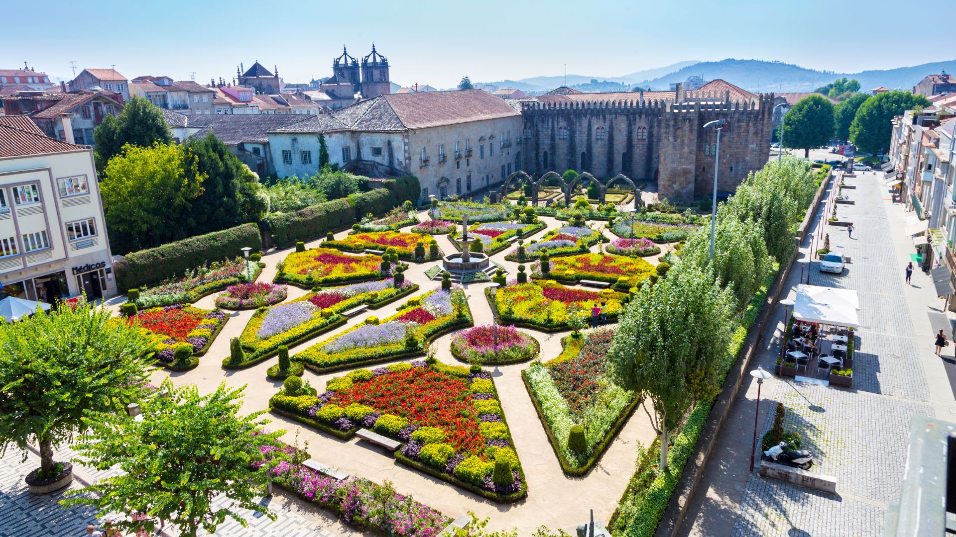 Aerial view of the vibrant Santa Barbara Garden in Braga, Portugal, featuring colorful flowerbeds, manicured hedges, and the historic Archbishop's Palace in the background."