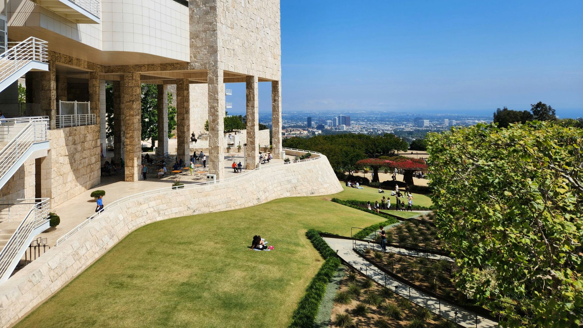 Panoramic view of the Getty Center in Los Angeles, featuring the modern museum architecture, lush green gardens, and the city skyline in the background under a clear sky.