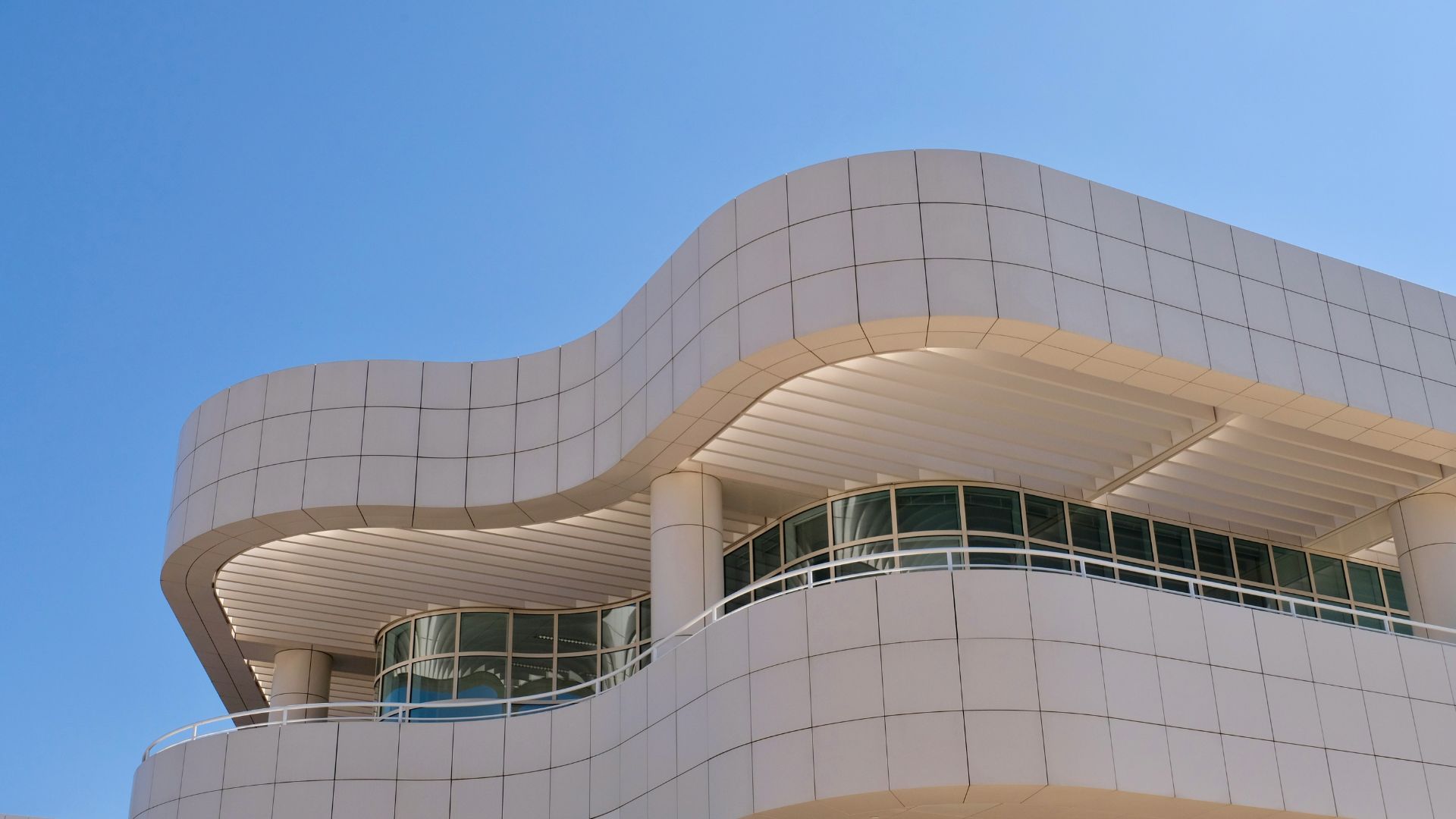 Modern architecture of the Getty Center in Los Angeles, featuring curved white walls, large windows, and balconies under a clear blue sky, showcasing the unique design of the museum and cultural complex.
