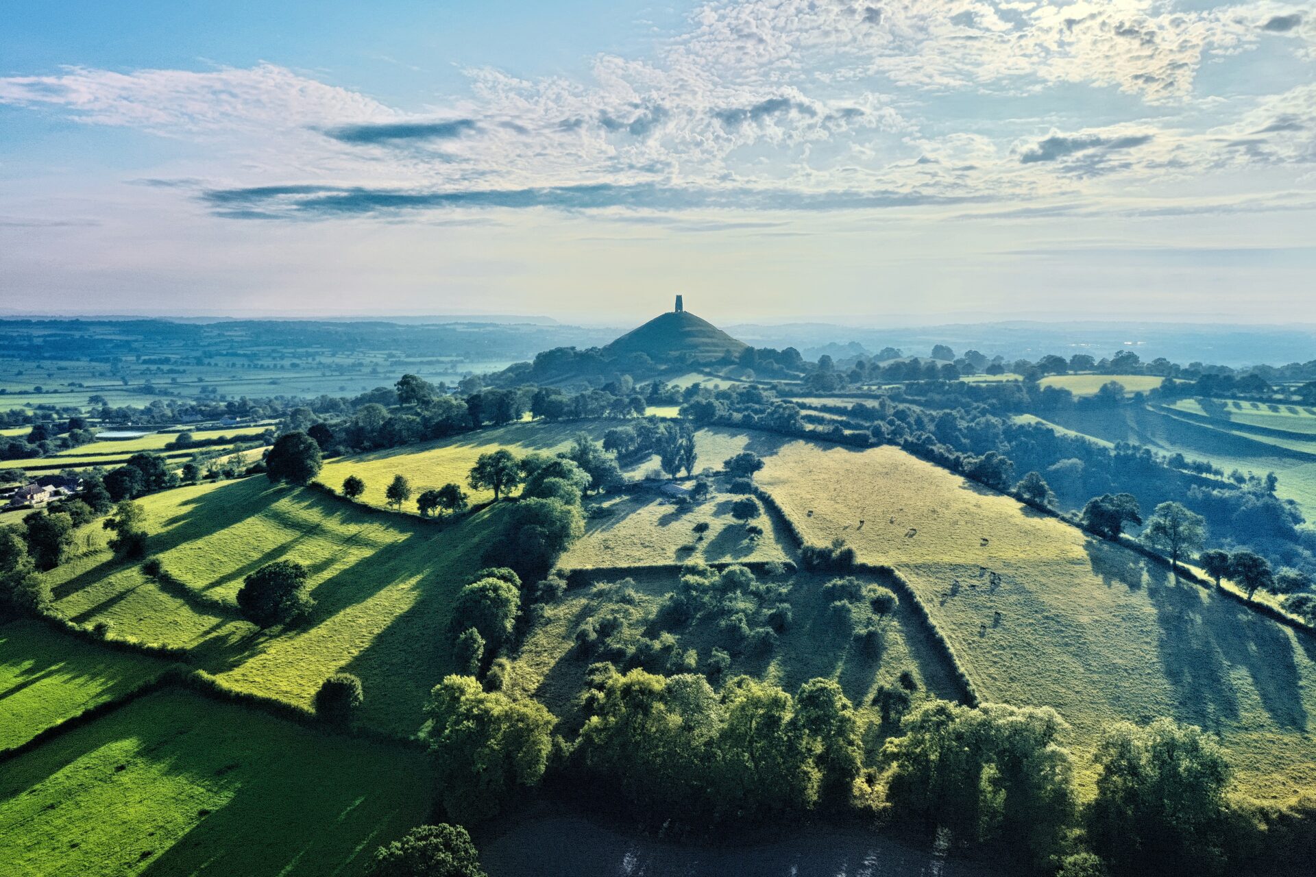 Glastonbury Tor, a hill with St. Michael's Tower at the summit, surrounded by rolling hills and lush countryside