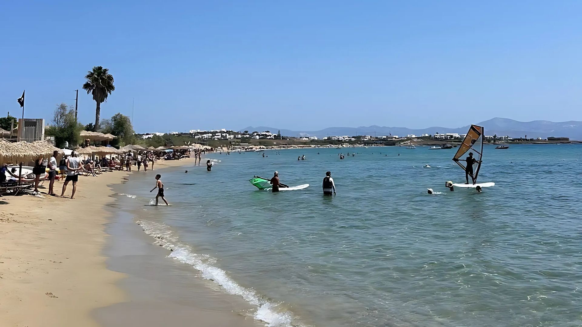 Golden Beach Paros, Greece, with windsurfers and clear blue water.
