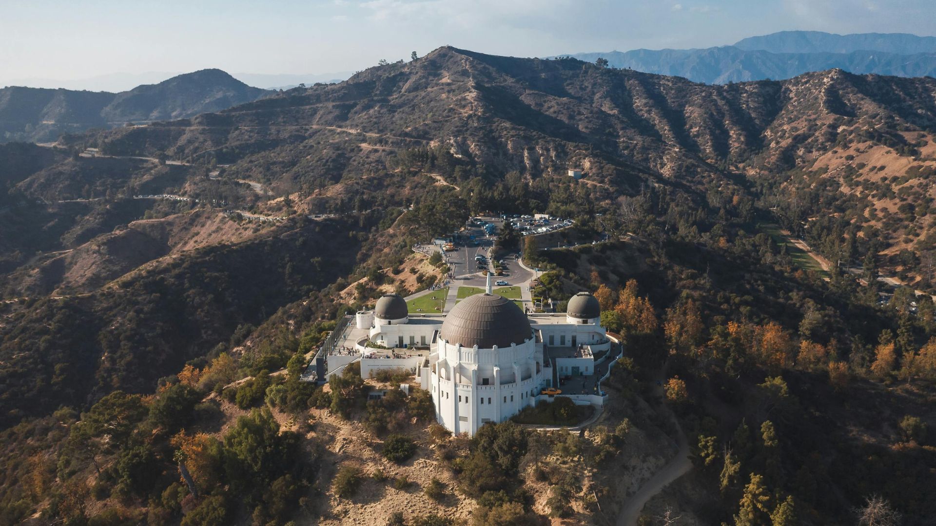 Aerial view of Griffith Observatory in Los Angeles, California, showcasing the iconic building, surrounding green lawns, and winding roads within Griffith Park.