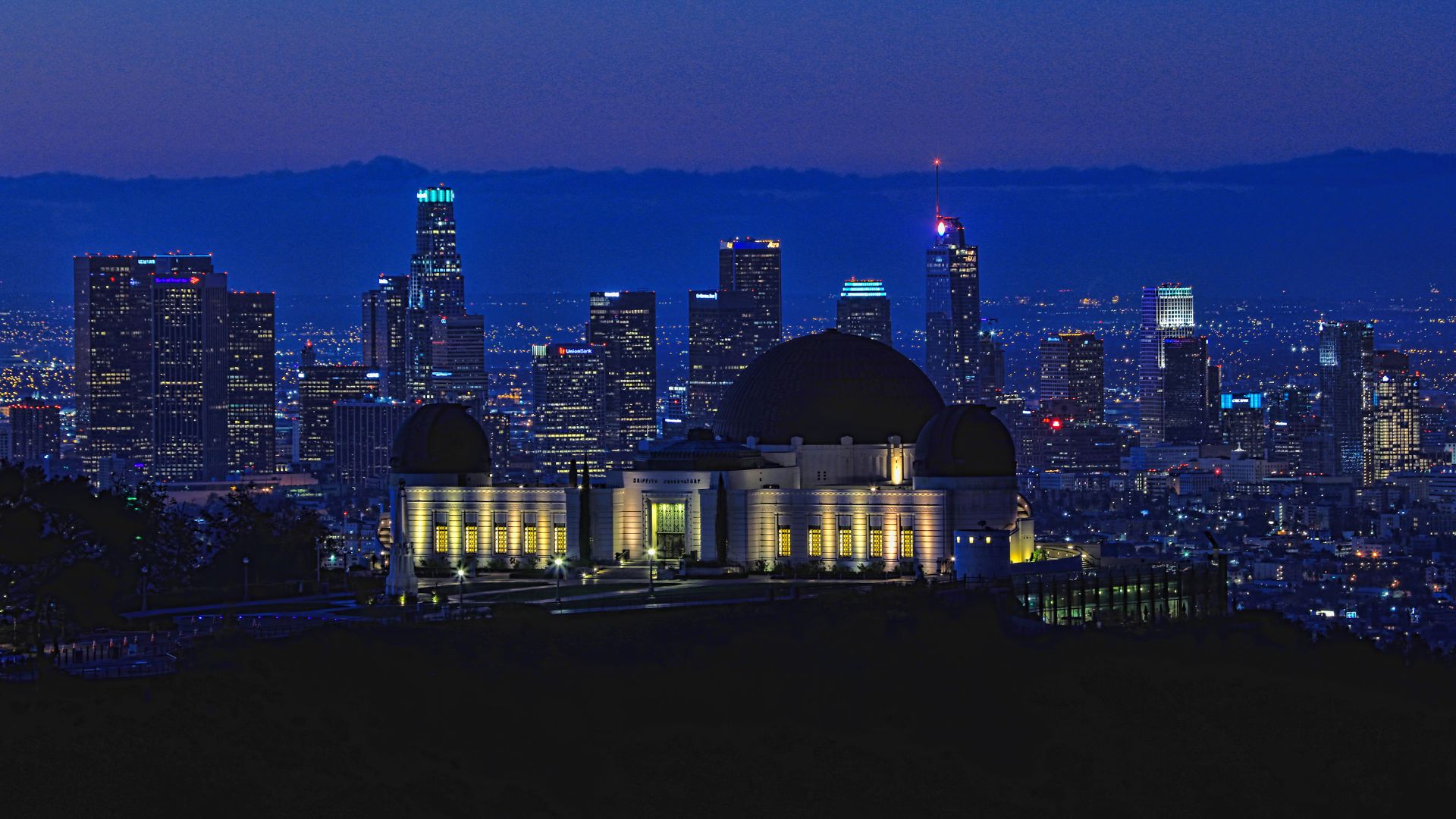 Aerial view of Griffith Observatory in Los Angeles, California, showcasing the iconic building, surrounding green lawns at night.
