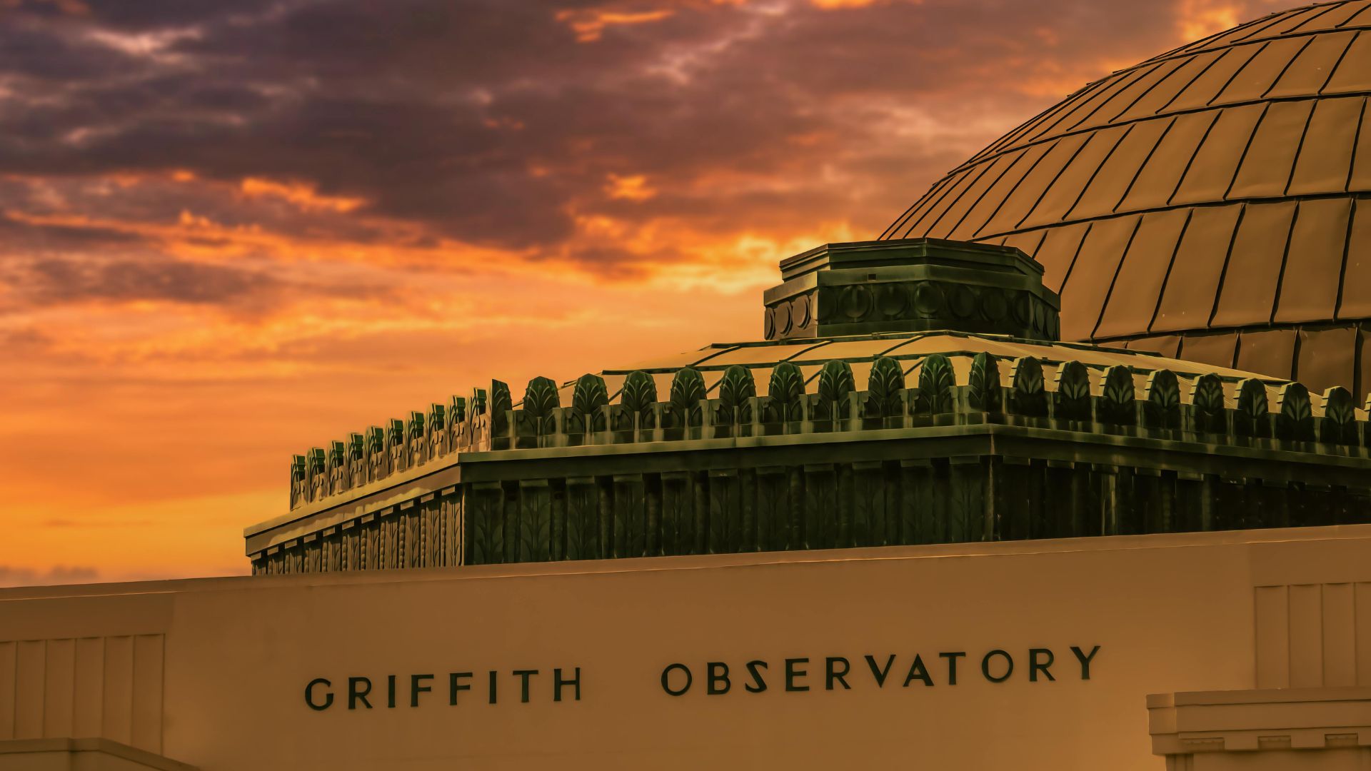 Griffith Observatory at sunset, featuring its iconic dome and building exterior against a vibrant orange and purple sky, with the observatory's name clearly visible on the facade. Ideal for showcasing Los Angeles landmarks and astronomy-related content.