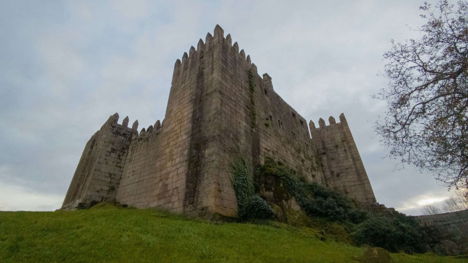 A low-angle shot of the historic Guimarães Castle in Portugal, showcasing its stone walls and crenellated towers against a clear blue sky.