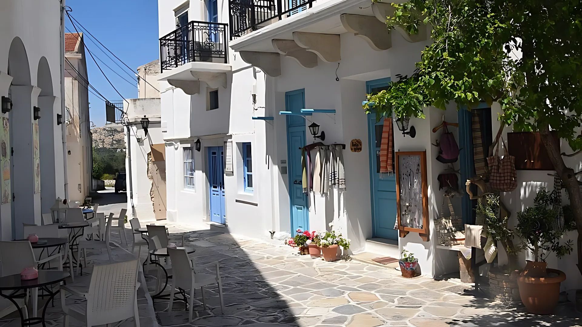 A charming village street in Chalkio, Naxos, with whitewashed buildings, blue doors, and outdoor seating.