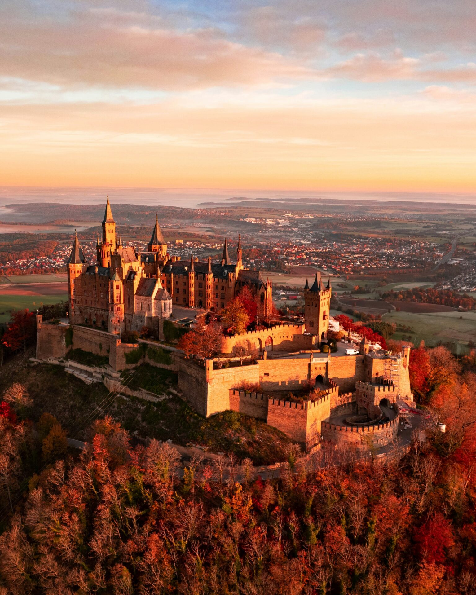 Hohenzollern Castle perched high above a golden-red forest canopy