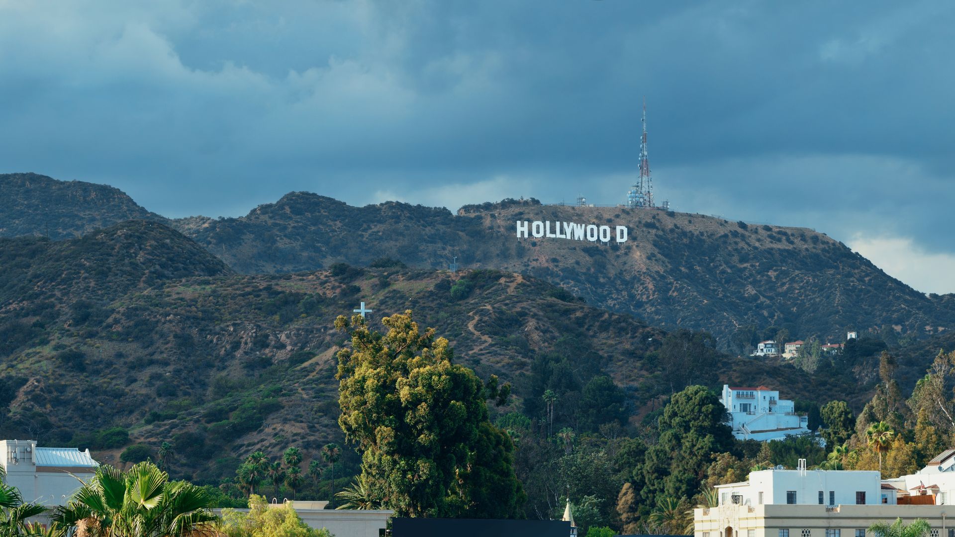 View of the Hollywood sign on Mount Lee, Los Angeles, with trees and buildings in the foreground.